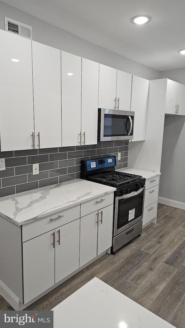 kitchen with appliances with stainless steel finishes, dark hardwood / wood-style floors, light stone countertops, decorative backsplash, and white cabinets