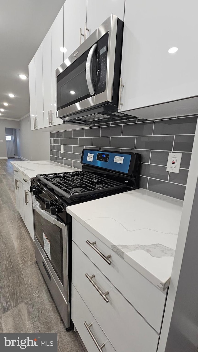 kitchen with dark hardwood / wood-style flooring, tasteful backsplash, light stone countertops, white cabinetry, and appliances with stainless steel finishes