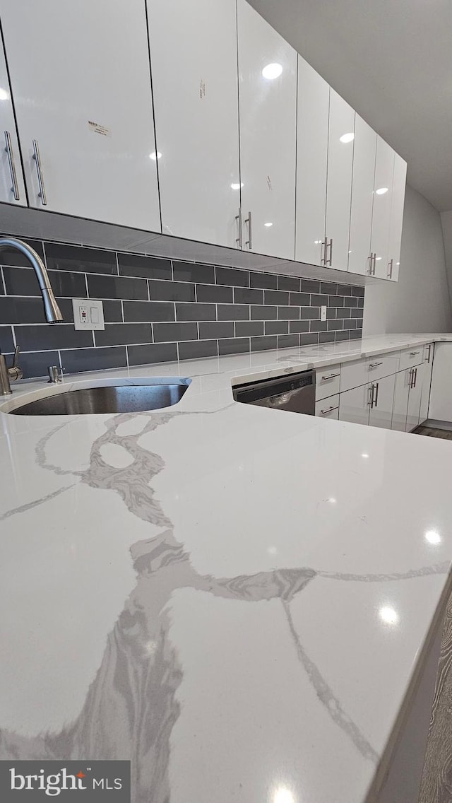 room details with dishwasher, sink, backsplash, light stone countertops, and white cabinetry