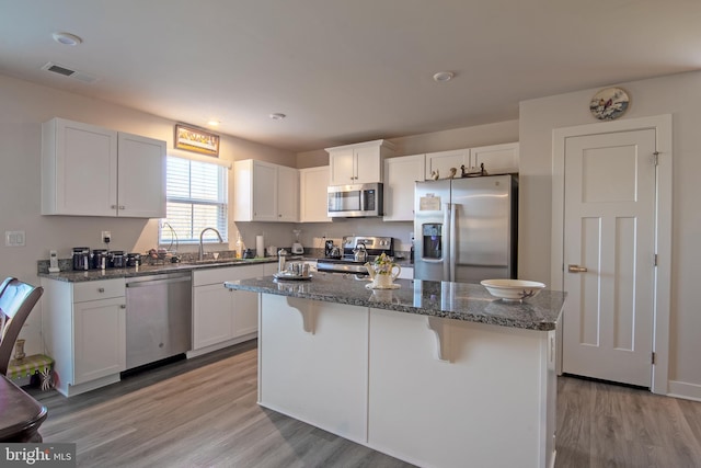 kitchen with stainless steel appliances, white cabinetry, dark stone countertops, a center island, and light wood-type flooring