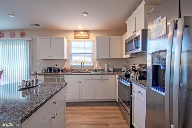 kitchen with white cabinetry, sink, appliances with stainless steel finishes, dark stone countertops, and light wood-type flooring