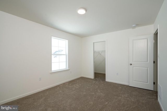 unfurnished bedroom featuring a walk in closet, a closet, and dark colored carpet