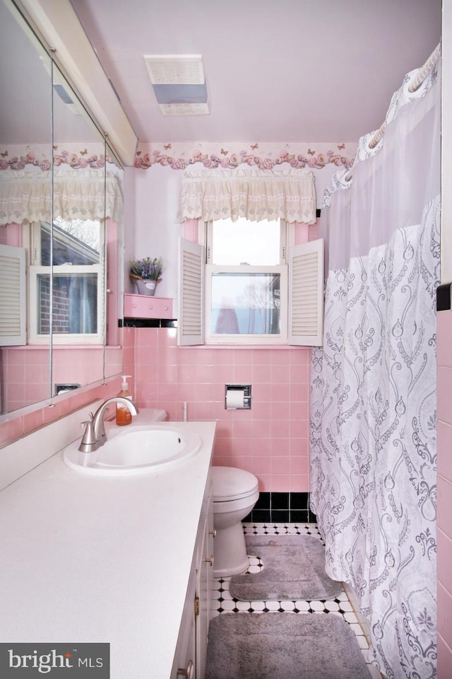 bathroom featuring tile patterned flooring, vanity, toilet, and tile walls