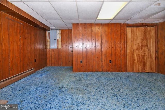 basement featuring carpet, a paneled ceiling, a baseboard heating unit, wooden walls, and electric panel