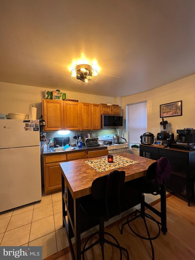 kitchen with white appliances, wooden counters, and light tile patterned floors