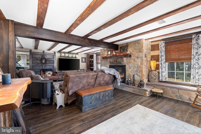 living room featuring a stone fireplace, dark wood-type flooring, beamed ceiling, and a barn door