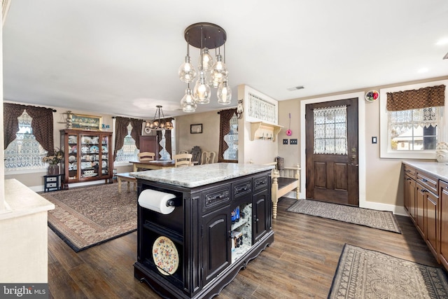 kitchen featuring a kitchen island, a notable chandelier, dark hardwood / wood-style floors, pendant lighting, and light stone countertops