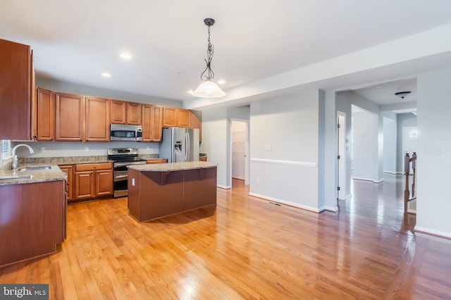 kitchen featuring a kitchen island, appliances with stainless steel finishes, pendant lighting, sink, and light hardwood / wood-style flooring