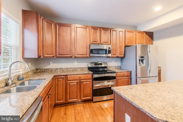 kitchen with light hardwood / wood-style floors, appliances with stainless steel finishes, sink, and light stone counters