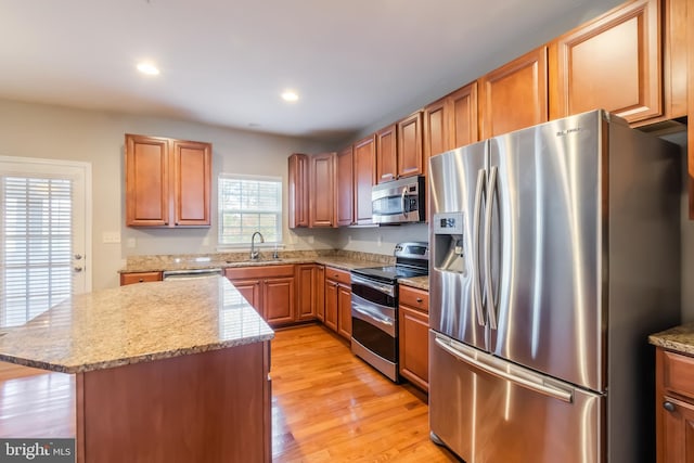 kitchen with light hardwood / wood-style floors, sink, appliances with stainless steel finishes, light stone countertops, and a center island