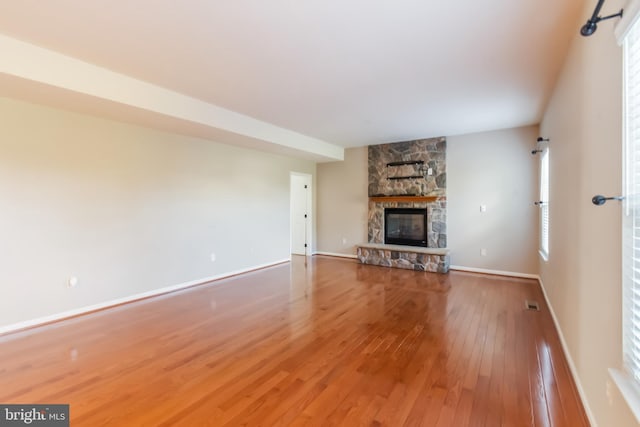 unfurnished living room featuring wood-type flooring and a stone fireplace