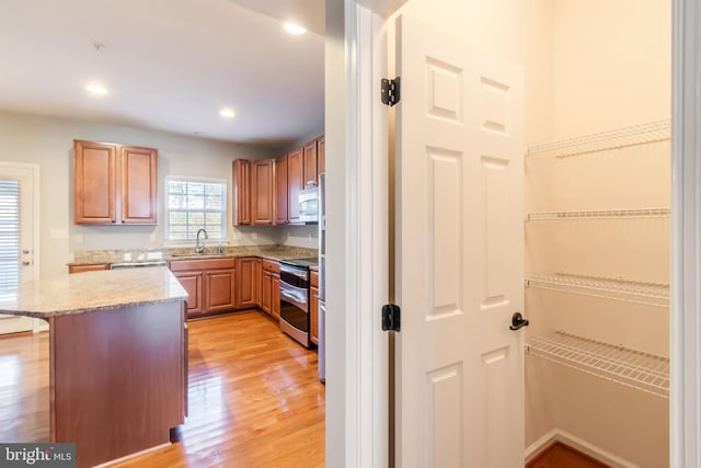 kitchen with stainless steel appliances, sink, a breakfast bar, light stone countertops, and light hardwood / wood-style flooring