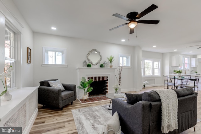 living room featuring ceiling fan, a brick fireplace, and light hardwood / wood-style flooring