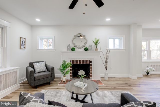 living room with radiator heating unit, light hardwood / wood-style floors, and a brick fireplace