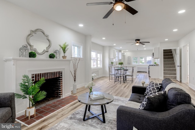 living room with a tiled fireplace, light hardwood / wood-style flooring, and ceiling fan