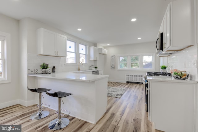 kitchen with radiator, stainless steel appliances, white cabinetry, light hardwood / wood-style floors, and kitchen peninsula