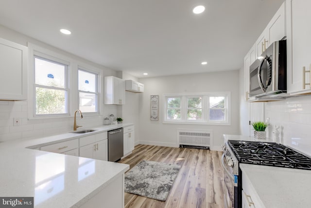 kitchen featuring radiator, light wood-type flooring, appliances with stainless steel finishes, and white cabinets