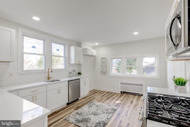 kitchen featuring stainless steel appliances, radiator, white cabinets, and sink