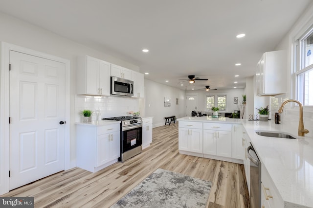 kitchen featuring stainless steel appliances, white cabinets, kitchen peninsula, sink, and light wood-type flooring