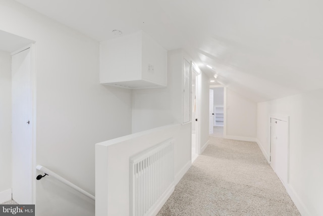 hall featuring radiator heating unit, light colored carpet, and vaulted ceiling