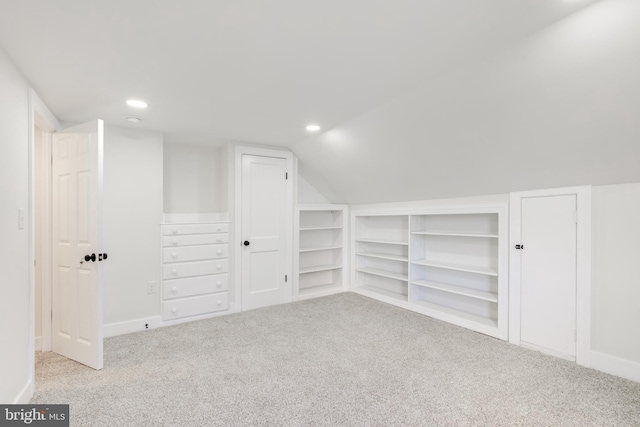 additional living space featuring built in shelves, light colored carpet, and lofted ceiling