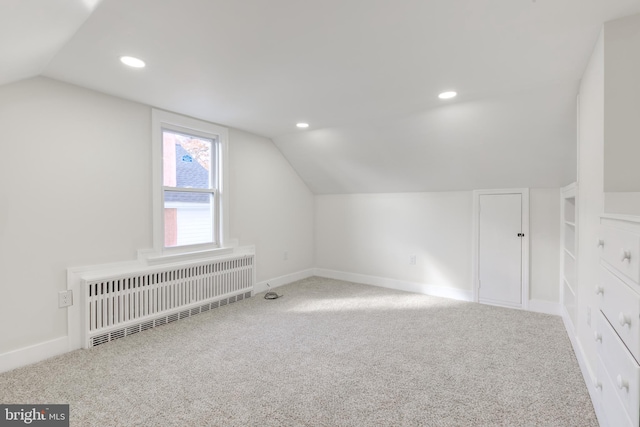 additional living space with radiator, lofted ceiling, and carpet floors