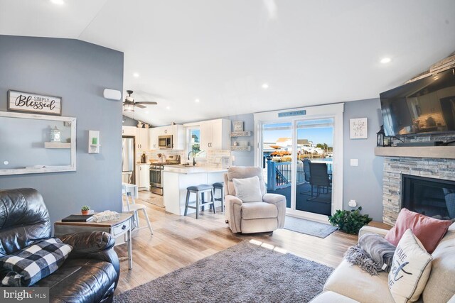 living room with a stone fireplace, light wood-type flooring, and lofted ceiling