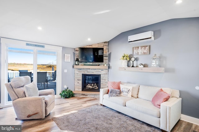 living room featuring a fireplace, a wall unit AC, wood-type flooring, and lofted ceiling