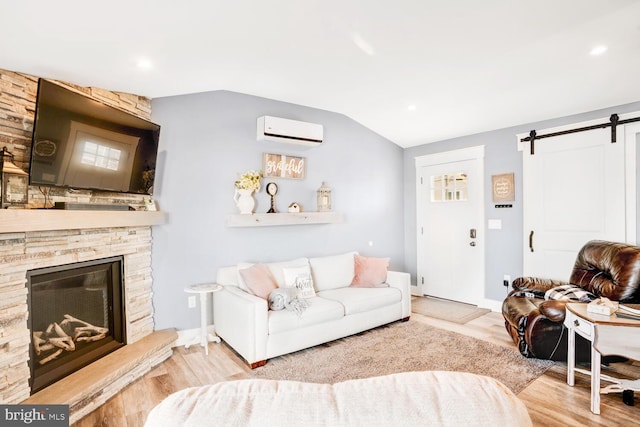 living room with light hardwood / wood-style floors, a stone fireplace, lofted ceiling, a barn door, and an AC wall unit