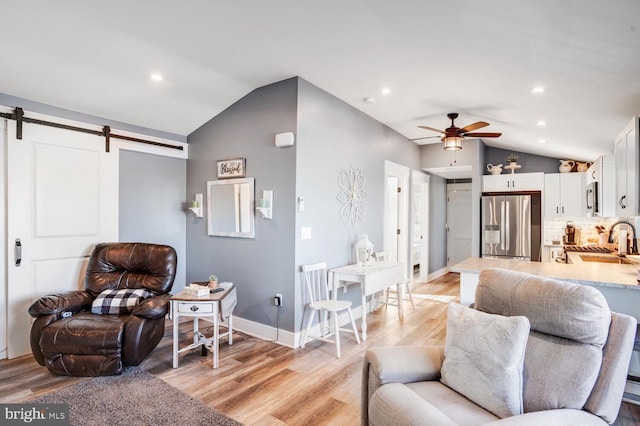 living room with light hardwood / wood-style floors, a barn door, and vaulted ceiling