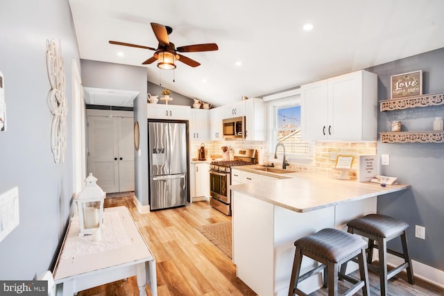 kitchen with stainless steel appliances, sink, a kitchen breakfast bar, white cabinets, and lofted ceiling