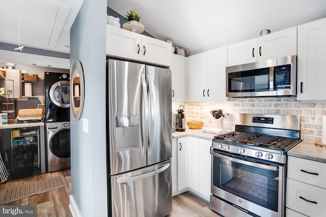 kitchen with white cabinets, light wood-type flooring, stainless steel appliances, and stacked washer and clothes dryer