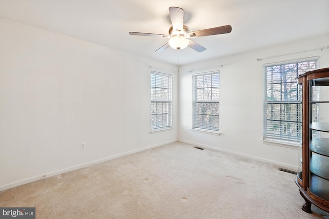 unfurnished room featuring ceiling fan, light carpet, and a wealth of natural light