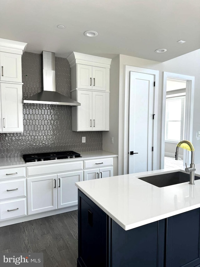 kitchen with wall chimney range hood, dark hardwood / wood-style flooring, decorative backsplash, sink, and white cabinets