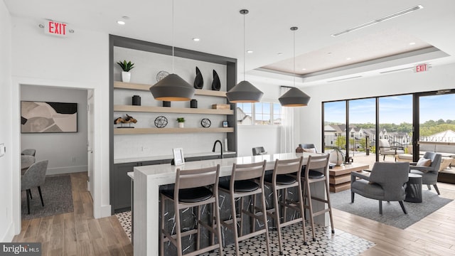 kitchen featuring light wood-type flooring, a kitchen bar, a raised ceiling, and pendant lighting