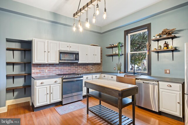 kitchen featuring stainless steel counters, light hardwood / wood-style flooring, backsplash, white cabinets, and appliances with stainless steel finishes