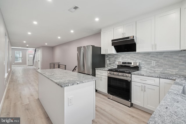 kitchen with white cabinetry, light stone counters, a center island, appliances with stainless steel finishes, and decorative backsplash