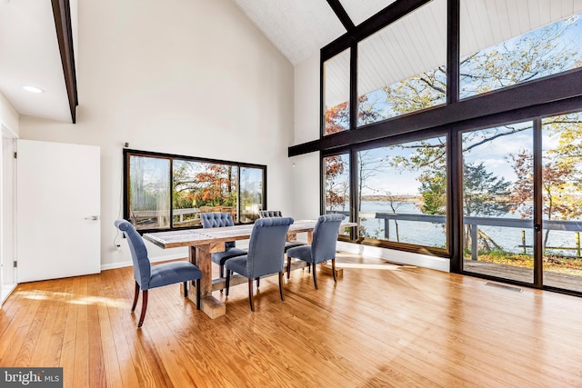 dining area featuring beamed ceiling, a water view, light wood-type flooring, and high vaulted ceiling