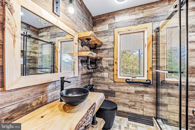 bathroom featuring toilet, a shower with shower door, wooden walls, and sink