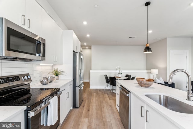 kitchen with sink, white cabinetry, light stone counters, appliances with stainless steel finishes, and pendant lighting