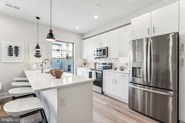 kitchen featuring appliances with stainless steel finishes, a breakfast bar, decorative light fixtures, white cabinets, and light hardwood / wood-style floors