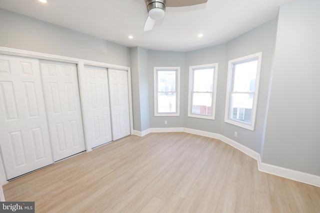 unfurnished bedroom featuring ceiling fan, light hardwood / wood-style flooring, and two closets