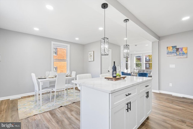 kitchen with hanging light fixtures, a center island, white cabinets, and light stone counters