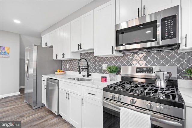 kitchen featuring sink, light stone counters, light wood-type flooring, appliances with stainless steel finishes, and white cabinets