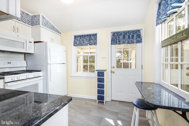 kitchen featuring lofted ceiling, white cabinets, dark stone counters, and white appliances