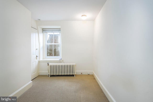 unfurnished room with radiator heating unit and light colored carpet