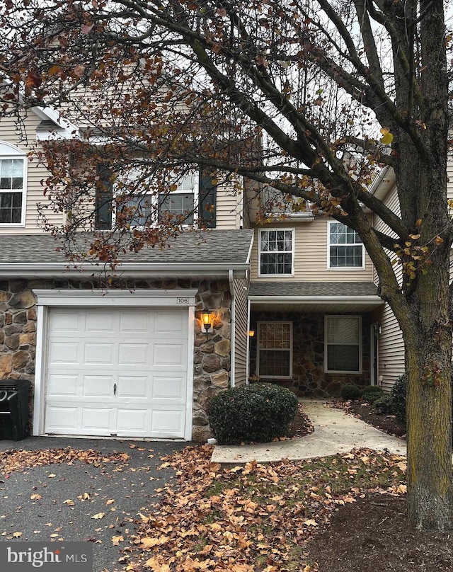 view of front of house with driveway, stone siding, an attached garage, and roof with shingles