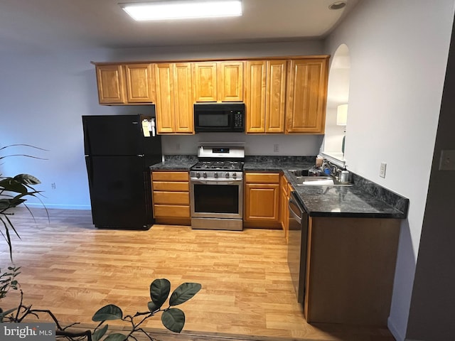 kitchen with black appliances, light hardwood / wood-style floors, sink, and dark stone counters