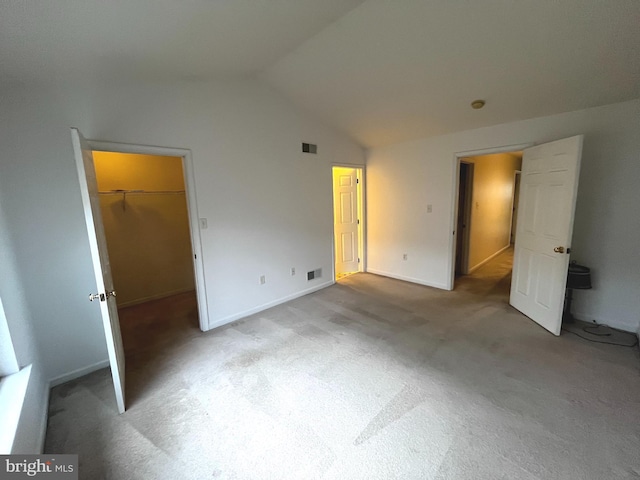 unfurnished bedroom with vaulted ceiling, light colored carpet, a spacious closet, and a closet