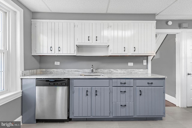 kitchen featuring a paneled ceiling, stainless steel dishwasher, sink, and gray cabinetry